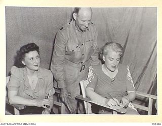 TOROKINA, BOUGAINVILLE, 1945-08-16. GRACIE FIELDS SIGNING AN AUTOGRAPH BOOK FOR MAJOR W.A. OLDFIELD BEFORE SHE COMMENCES ENTERTAINING TROOPS AT HEADQUARTERS 2 CORPS. MISS PEGGY SHEA (1) IS ONE OF ..