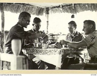 THE DINING ALCOVE OF THE AUSTRALIAN NEW GUINEA ADMINISTRATIVE UNIT NON COMMISSIONED OFFICERS' HUT. THE TABLE IS CONSTRUCTED FROM A TYPE OF NATIVE CAMPHOR WOOD. IDENTIFIED PERSONNEL ARE: NX191070 ..