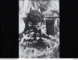 MARUKINAM RIVER, NEW GUINEA. 1944-05-28. NX120502 CORPORAL F. E. BROWN, 35TH INFANTRY BATTALION, BLOWING ON A FIRE TO BOIL BILLY TEA IN AN OPERATION RATION TIN AT GURUM, DURING THE PUSH TOWARDS ..