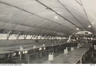 Numbered wooden tables and benches lined up in the large domed interior of the Japanese prisoner's cafeteria at the RAN War Criminal Compound at an RAN shore base. Work on this RAN base commenced ..