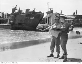 SERGEANT I. STOCKDALE (LEFT) AND LIEUTENANT G. GOODFELLOW (RIGHT), MEMBERS OF 7 DOCKS OPERATING COMPANY, ROYAL AUSTRALIAN ENGINEERS, DISCUSSING CARGO AND LOADING OPERATIONS FOR THE LANDING CRAFT ..