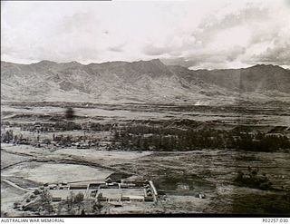 Garoka, New Guinea, 1945-11. Aerial view of the RAAF Aircrew Rest Camp (bottom) which is known as 'Lamana', meaning 'Eternal Springs', with the peaks of tall hills or mountains rising in the ..