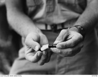 MILILAT, NEW GUINEA. 1944-07-16. A MEMBER OF THE 1ST PIGEON SECTION, HEADQUARTERS, 5TH DIVISION DEMONSTRATES THE METHOD OF PLACING A MESSAGE IN THE SPECIAL CAPSULE ATTACHED TO THE PIGEON'S LEG