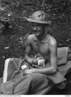 DUMPU, NEW GUINEA, 1943-10-15. VX75884 PRIVATE K. KILPATRICK OF NORTHCOTE, VIC, A PATIENT OF THE 2/6TH AUSTRALIAN FIELD AMBULANCE SHOWING HIS TIN HAT WHICH WAS RIDDLED BY FRAGMENTS OF A JAPANESE ..