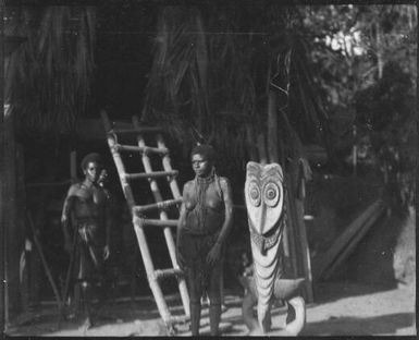 Woman standing beside a  house ladder and a carved piece of timber, Tambunum, Sepik River, New Guinea, 1935 / Sarah Chinnery