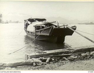 MILNE BAY, NEW GUINEA. 1944-04-06. A CAPTURED JAPANESE BARGE MARKED AB588 IN USE AS A CARGO CARRYING VESSEL. ALLIED SHIPPING LIE IN ANCHORAGE AT THE BACKGROUND