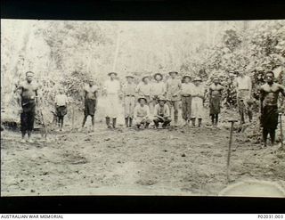 Bitapaka, New Britain. 1915-01-05. Group portrait of RAN members of the Australian Naval and Military Expeditionary Force (AN&MEF) and (indigenous) New Briton natives standing behind a pipe mine ..