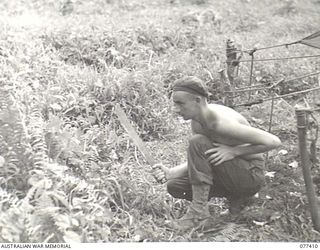 MALMAL MISSION, JACQUINOT BAY, NEW BRITAIN. 1944-11-30. N377688 PRIVATE M.S. GLANVILLE, HEADQUARTERS, 5TH DIVISION USING A MACHETE TO CLEAR AWAY JUNGLE UNDERGROWTH FROM THE UNIT TENT LINES