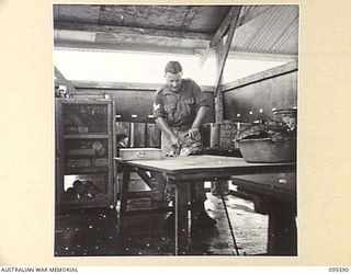 CAPE WOM, WEWAK AREA, NEW GUINEA. 1945-08-28. SERGEANT M.J. LAWRENCE, 104 CASUALTY CLEARING STATION PREPARING MEAT IN THE HOSPITAL KITCHEN FOR PATIENTS