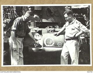 VX24274 MAJOR R. H. HODGES (1) AND SX23760 LIEUTENANT G. H. TIVER (2) OF THE 1ST TANK BATTALION GROUP WORKSHOPS, AUSTRALIAN ELECTRICAL AND MECHANICAL ENGINEERS, EXAMINING THE EFFECTS OF SHELLFIRE ..