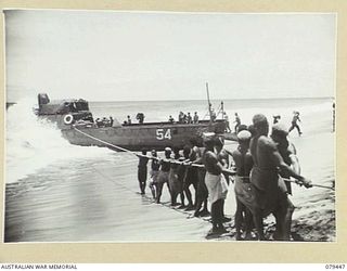 BOUGAINVILLE ISLAND. 1945-03-06. NATIVES PULLING ON A QUARTER LINE ATTACHED TO A LANDING BARGE WHICH IS TRYING TO LAND SUPPLIES AT THE NEW HEADQUARTERS OF THE 7TH INFANTRY BRIGADE AT TOKO. OWING TO ..