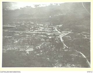 PIVA STRIP, TOROKINA, BOUGAINVILLE, SOLOMON ISLANDS. 1945-03-12. PIVA STRIP AND SURROUNDING BUILDINGS VIEWED AS A SUPPLY DROPPING AIRCRAFT RETURNS TO RE-LOAD WITH CARGO. PERSONNEL OF THE 121ST ..