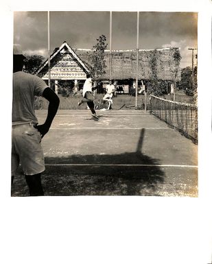 Photo of men playing tennis with a traditional hut in the background.