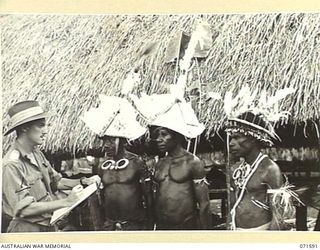 SONG RIVER, FINSCHHAFEN AREA, NEW GUINEA. 1944-03-26. N181937 LIEUTENANT E. H. D. WATSON (1), AND OFFICIAL WAR ARTIST SKETCHING NATIVES WEARING HEADDRESS USED FOR A SING-SING AT THE AUSTRALIAN NEW ..