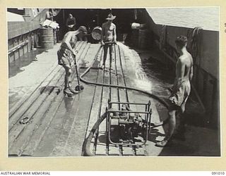 JACQUINOT BAY, NEW BRITAIN. 1945-04-17. 41 LANDING CRAFT COMPANY PERSONNEL USE A PORTABLE POWER PUMP ABOARD THE BARGE AB2027 TO SWAB DOWN THE DECKS, THEIR LAST TASK BEFORE A WELL EARNED REST. ..