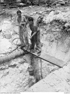 MOMOTE, LOS NEGROS ISLAND, ADMIRALTY ISLANDS. C. 1944-03. TWO MEMBERS OF THE GROUND STAFF OF NO. 79 (SPITFIRE) SQUADRON RAAF HAULING UP A BUCKET OF WATER IN THE PROCESS OF SERVICING AND BUILDING ..