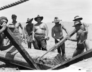 ANAMO AREA, NEW GUINEA. 1944-11-23. TROOPS OF THE 2/2 FIELD COMPANY, ROYAL AUSTRALIAN ENGINEERS, LEVER LOGS INTO POSITION FOR THE ERECTION OF DECK SUPPORTS DURING BRIDGE CONSTRUCTION AT AN UNNAMED ..