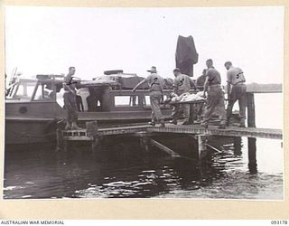 BOUGAINVILLE, 1945-06-18. MEMBERS OF 1 WATER AMBULANCE CONVOY, CARRYING A CASUALTY IN A THOMAS SPLINT, TO A WAITING BOAT, DURING THE EVACUATION OF WOUNDED BY WATER FROM MOTUPENA POINT, GAZELLE ..