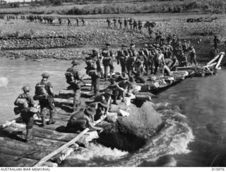 1943-10-21. NEW GUINEA. RAMU VALLEY. AUSTRALIAN TROOPS IN THEIR VICTORIOUS PUSH ALONG THE MARKHAM AND RAMU VALLEYS CROSS A BRIDGE OVER THE TEN KNOT GUSAP RIVER. THIS BRIDGE WAS BUILT IN A FEW ..