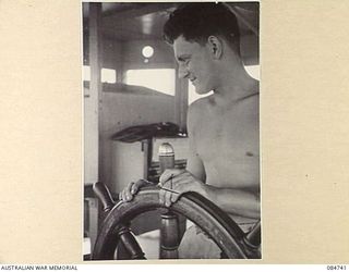 MADANG, NEW GUINEA. 1944-11-06. ABLE SEAMAN MCGUINESS AT THE WHEEL ABOARD HMAS STAWELL