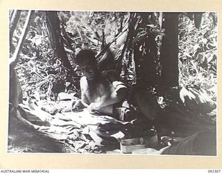 BOUGAINVILLE, 1945-05-18. PRIVATE W. GOUDIE, MORTAR PLATOON, 57/60 INFANTRY BATTALION, TAKES ADVANTAGE OF TIME OFF TO HAVE A READ IN HIS "DOOVER". IT IS ON THE BANKS OF THE HUDA RIVER AND IS ..