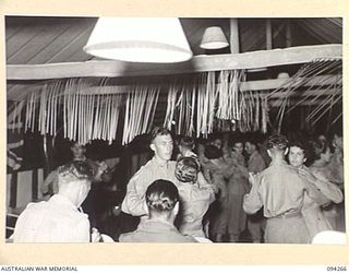 LAE AREA, NEW GUINEA. 1945-07-24. A SECTION OF THE 2/1 GUARD REGIMENT BAND (IN THE FOREGROUND) PLAYING DURING A DANCE HELD BY THE STAFF OF THE AUSTRALIAN ARMY CANTEEN SERVICES