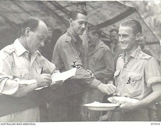 MALMAL MISSION, JACQUINOT BAY, NEW BRITAIN. 1944-11-30. CORPORAL R. TAYLOR (2) ISSUING THE DAILY ATEBRIN TABLETS TO DRIVER STANTON (3) SUPERVISED BY CAPTAIN JENKINS AT THE EVENING MESS PARADE OF ..