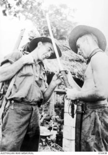 Nanda, Huon Peninsula, New Guinea. 1 January 1944. Corporal J. Holloway (left) of Summerset, Qld, admires a Japanese sword found by Sergeant K. B. McDonald of Casino, NSW, after the hasty ..