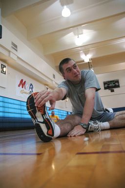 US Navy (USN) Store Keeper 2nd Class (SK2) Kevan Lamb does a "runner's stretch" at the beginning of group Physical Training (PT) in the Charles King Gym at Naval Base (NB) Guam (GU). SK2 Lamb is attached to the Supply Department of Submarine Squadron 15, the Navys only forward-deployed fast-attack submarine squadron