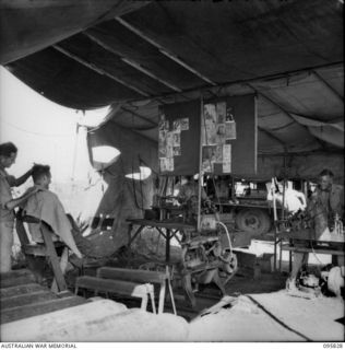 CAPE WOM, WEWAK AREA, NEW GUINEA. 1945-08-29. CRAFTSMAN F. DAVIS SEATED IN CHAIR AT BARBER'S SHOP, 110 BRIGADE WORKSHOP, CORPS OF AUSTRALIAN ELECTRICAL AND MECHANICAL ENGINEERS