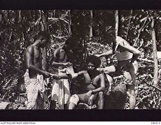 REINHOLD HIGHWAY, NEW GUINEA, 1943-08-31. OVA, A NATIVE "LIK-LIK-DOCTOR" BANDAGING A PATIENT'S ARM UNDER THE SUPERVISION OF WARRANT OFFICER M. C. MANN, AUSTRALIAN AND NEW GUINEA ADMINISTRATION UNIT