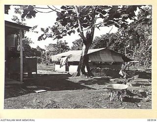 LAE, NEW GUINEA. 1944-12-12. THE STAFF SLEEPING QUARTERS AT THE ARMY CANTEENS SERVICE SOFT DRINK FACTORY WITHIN LAE BASE SUB-AREA, WITH EMPTY BOTTLES STACKED AT THE FOREGROUND AND A JUNGLE LINED ..