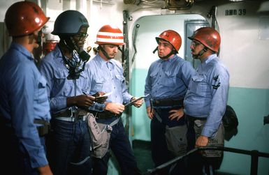 Members of a firefighting team and a repair party member go over instructions prior to taking part in a drill aboard the amphibious assault ship USS GUAM (LPH 9). The repair party member is equipped with a sound-powered phone