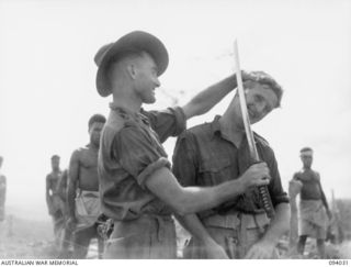 WEWAK AREA, NEW GUINEA, 1945-07-14. PTE H. DOHERTY, A COMPANY, 2/8 INFANTRY BATTALION (1) DEMONSTRATING THE "SHARPNESS" OF A JAPANESE SWORD ON CPL T. FERNIHOUG (2), WHO IS IN CHARGE OF 2/8 ..