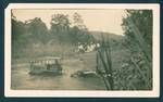 Tractor crossing river, pulling load of timber, four Europeans and three New Guineans sit on top of timber, New Guinea, c1929 to 1932