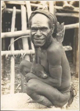 Types from villages of Evese, Ononge [man squatting and holding a pig]