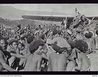 WABAG, NEW GUINEA. NATIVES SURROUND THE FIRST AEROPLANE TO LAND AT WABAG WITH SUPPLIES FOR THE TAYLOR AND BLACK EXPEDITION. THE AIRCRAFT, A FORD TRIMOTOR, WAS REQUISITIONED BY THE RAAF ON THE ..