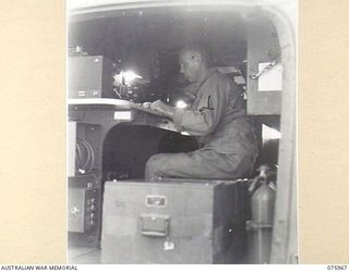 MILILAT, NEW GUINEA. 1944-09-15. MASTER-SERGEANT R.G. FREEMAN, RADIO OPERATOR, UNITED STATES ARMY GENERAL HEADQUARTERS DETACHMENT ATTACHED TO 5TH DIVISION, WORKING IN THE UNIT RADIO TRUCK