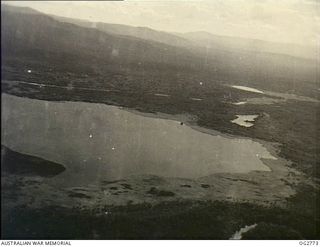 NEW GUINEA. C. 1944. AERIAL PHOTOGRAPH OF A BAY SURROUNDED BY JUNGLE AND MOUNTAINS