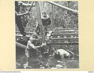 LAE, NEW GUINEA. 1943. AUSTRALIAN ENGINEERS CONSTRUCTING A PREFABRICATED BRIDGE UNDER DIFFICULTIES