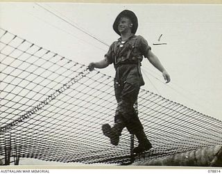 DANMAP RIVER, NEW GUINEA. 1945-01-26. A MEMBER OF THE AUSTRALIAN MILITARY FORCES CROSSING AN IMPROVISED BRIDGE ACROSS THE RIVER. THE DECKING OF THIS BRIDGE CONSISTS OF A LONG STRIP OF STEEL MESH ..