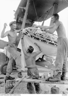 JACQUINOT BAY, NEW BRITAIN. 1945-04-12. A SUPERMARINE WALRUS AMPHIBIAN AIRCRAFT USED BY NO. 10 COMMUNICATIONS FLIGHT RAAF, HAS ITS WING FABRIC REPAIRED BY AIRMEN. LEFT TO RIGHT: 19354 CORPORAL ..