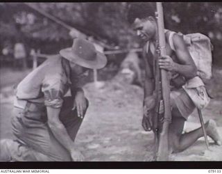 TSIMBA AREA, BOUGAINVILLE ISLAND. 1945-02-19. ANTON, A WHITE CIVILIAN (LEFT) AND A MEMBER OF THE NEW GUINEA CONSTABULARY CHECKING TRACKS ON THE BEACH WHILE SEARCHING FOR JAPANESE DURING AN ..