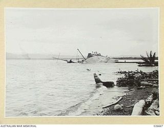 MILNE BAY, PAPUA. 1942-09. THE STEAMER "ANSHUN" LYING ON HER SIDE IN MILNE BAY, WHERE SHE WAS SHELLED AND SUNK BY A JAPANESE CRUISER. THE "ANSHUN" WAS LATER SALVAGED AND TOWED TO SYDNEY, A DISTANCE ..