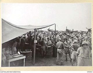 JACQUINOT BAY, NEW BRITAIN, 1945-08-23. TROOPS LINED UP AT THE TOTE FOR BETS AT THE ROYAL NEW ZEALAND AIR FORCE VICTORY CUP RACE MEETING. THE NEW ZEALANDERS ORGANISED THE MEETING USING WOODEN ..