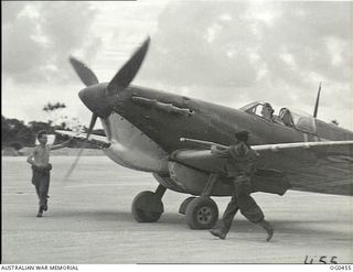 KIRIWINA, TROBRIAND ISLANDS, PAPUA. 1944-01-11. TWO FITTERS JUMP FROM THE WING OF A SPITFIRE AIRCRAFT OF NO. 79 (SPITFIRE) SQUADRON RAAF AS PILOT OFFICER LES MCKELLAR OF GUNNEDAH, NSW, PREPARES TO ..