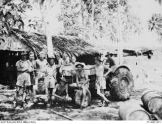 The A Flight armourers of  No. 100 Squadron RAAF gathered around a tractor in front of the section's palm-roofed hut at Gurney Airfield. Left to right: back row: Ian Smith; Keating; Ian ..