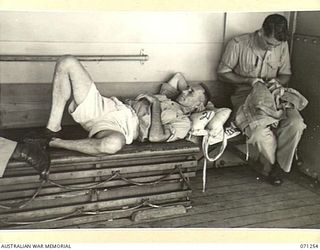 AT SEA, 1944-03. VX107875 STAFF-SERGEANT R. ANDERSON (1), DOES SOME SEWING, WHILST PETTY OFFICER E. COE, ROYAL AUSTRALIAN NAVY (2), SLEEPS RESTING ON A LIFE JACKET ABOARD THE TROOPSHIP HT TAROONA ..