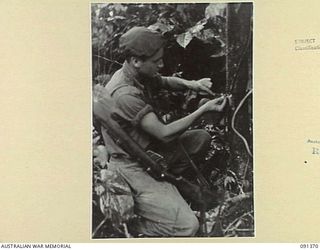 BOUGAINVILLE. 1945-04-30. LANCE CORPORAL L.T. DAGAN, 9 INFANTRY BATTALION SETTING A MURRAY SWITCH TO WHICH IS ATTACHED A TRIP WIRE. WHEN THE WIRE IS FOULED A .303 CHARGE DETONATES AS AN ALARM. THE ..