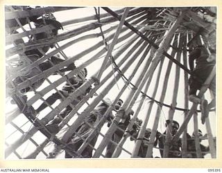 KIARIVU, WEWAK AREA, NEW GUINEA, 1945-08-12. AUSTRALIAN NEW GUINEA ADMINISTRATIVE UNIT NATIVES AT WORK ON THE CIRCULAR ROOF OF THE HUT TO BE USED AS AUSTRALIAN NEW GUINEA ADMINISTRATIVE UNIT ..